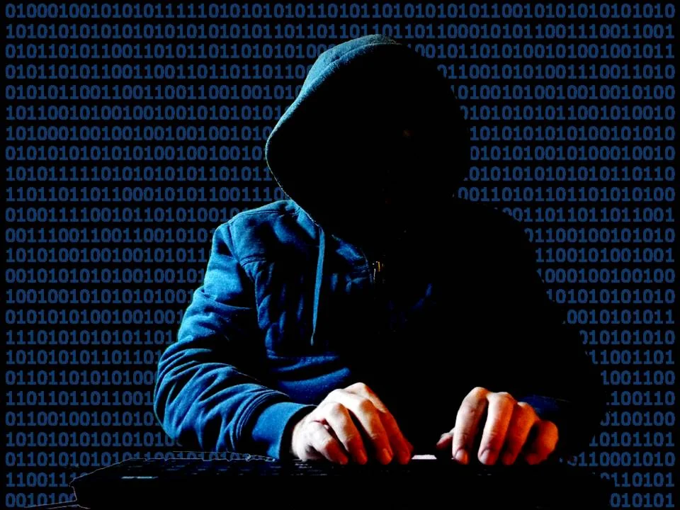 Pirate informatique encapuchonné devant un clavier avec du code binaire