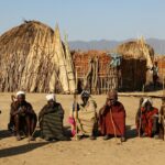 group of tribal men sitting on soil while holding sticks